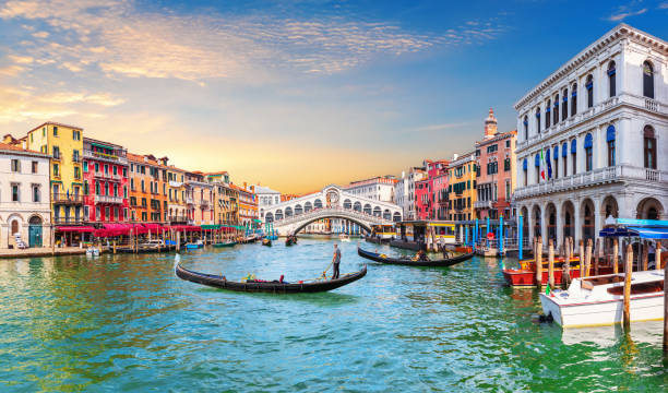 A scenic view of the white stone Rialto Bridge spanning the Grand Canal in Venice, Italy, with several traditional black gondolas floating on the water - Image by istockphoto.com.